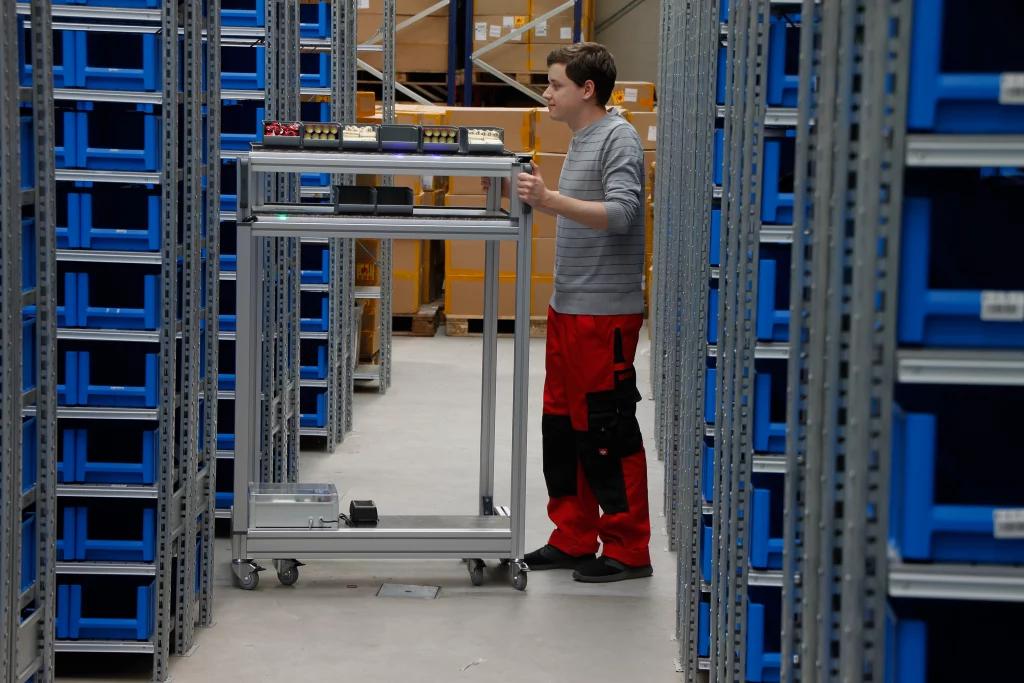 Ein Mitarbeiter schiebt den Pick Cart Kommissionierwagen dank Put-to-Light Technologie routenoptimiert ans Ziel.